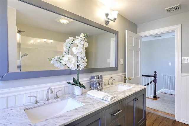 full bath with double vanity, visible vents, a sink, and wood finished floors