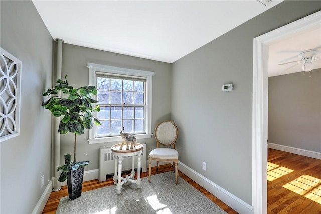 sitting room featuring a ceiling fan, radiator, baseboards, and wood finished floors