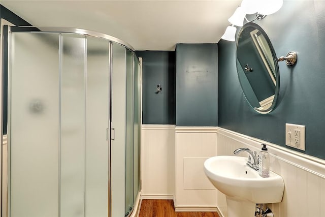 bathroom with a wainscoted wall, a stall shower, a sink, and wood finished floors