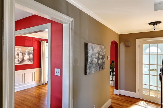 hallway with ornamental molding, arched walkways, baseboards, and wood finished floors