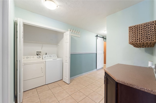 clothes washing area with laundry area, a barn door, light tile patterned floors, and washer and clothes dryer