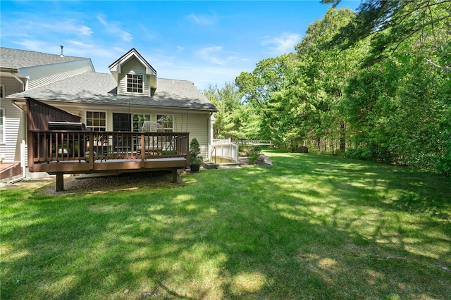 rear view of property featuring a deck, a yard, and roof with shingles