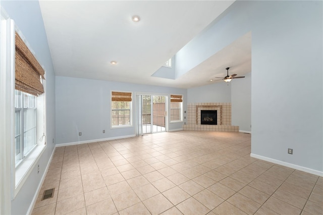 unfurnished living room featuring lofted ceiling, ceiling fan, light tile patterned floors, visible vents, and a tiled fireplace