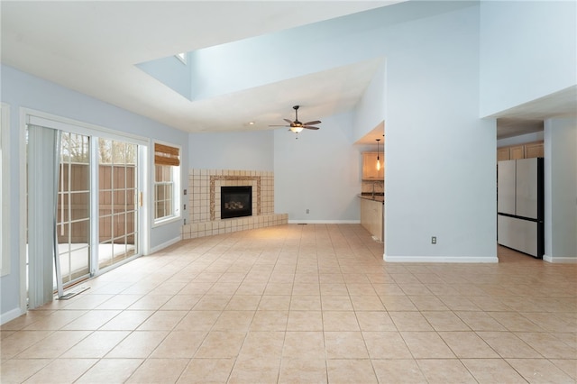 unfurnished living room with baseboards, a ceiling fan, a tiled fireplace, high vaulted ceiling, and light tile patterned flooring