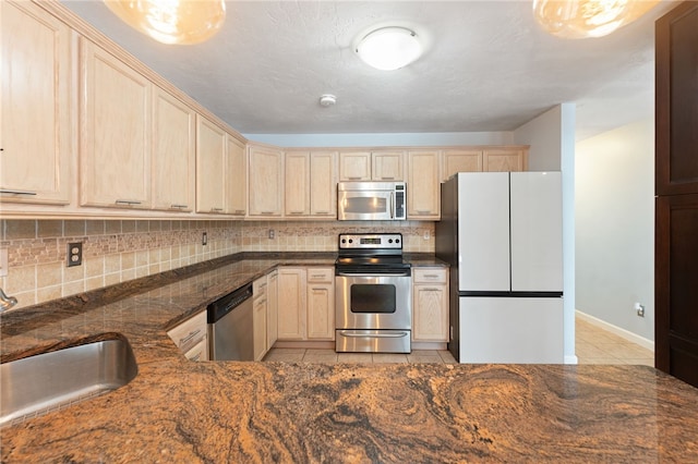 kitchen with light tile patterned floors, dark stone counters, a sink, stainless steel appliances, and backsplash