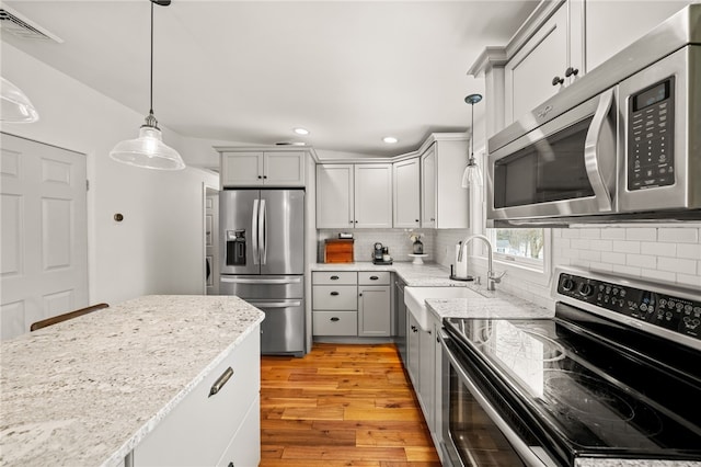 kitchen with appliances with stainless steel finishes, light wood-type flooring, a sink, and decorative backsplash