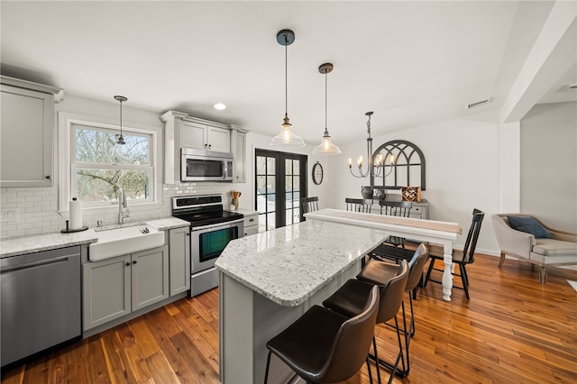 kitchen with backsplash, gray cabinets, stainless steel appliances, and a sink