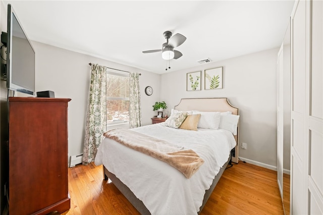 bedroom with visible vents, a baseboard heating unit, a ceiling fan, light wood-type flooring, and baseboards