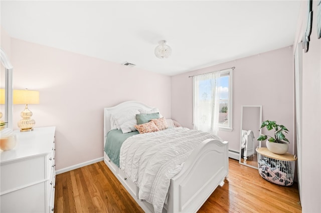 bedroom with baseboards, baseboard heating, visible vents, and light wood-style floors