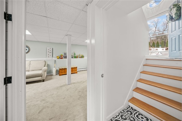 stairway with a baseboard heating unit, carpet floors, a paneled ceiling, and baseboards