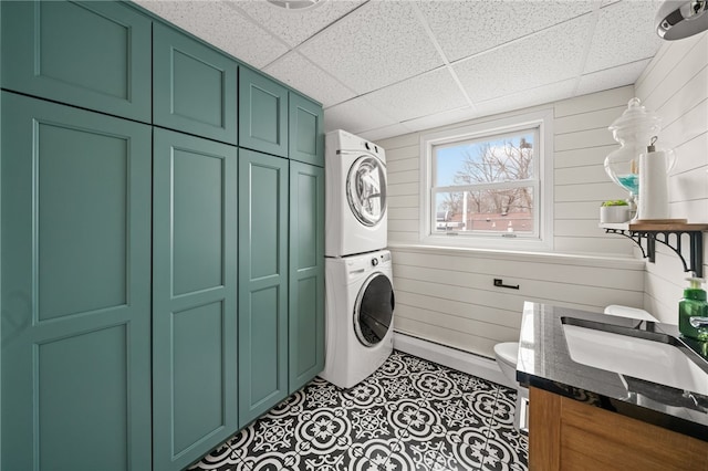 washroom with wooden walls, a sink, stacked washing maching and dryer, cabinet space, and tile patterned floors