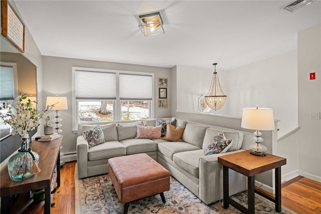 living area featuring a baseboard radiator, visible vents, an inviting chandelier, wood finished floors, and baseboards