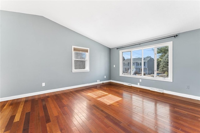 empty room featuring lofted ceiling, hardwood / wood-style floors, visible vents, and baseboards