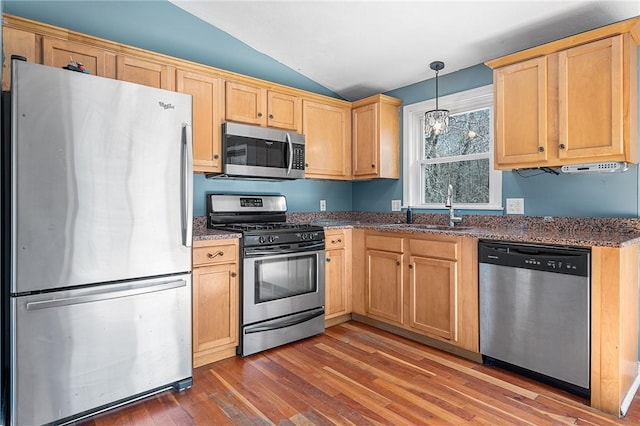 kitchen with wood finished floors, a sink, vaulted ceiling, appliances with stainless steel finishes, and dark stone counters