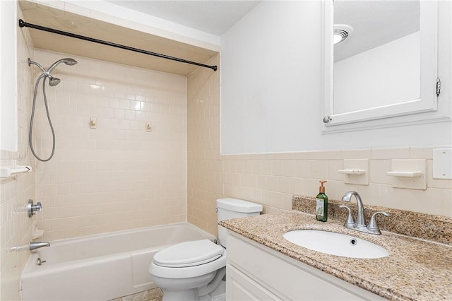 bathroom featuring wainscoting, toilet, vanity, tile walls, and shower / bathing tub combination