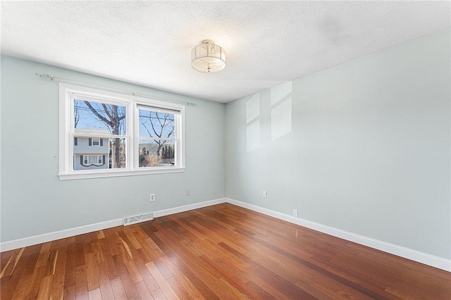 spare room featuring a textured ceiling, hardwood / wood-style floors, visible vents, and baseboards