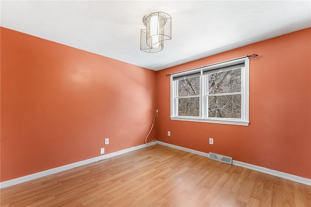 spare room with light wood-style flooring, a textured ceiling, visible vents, and baseboards