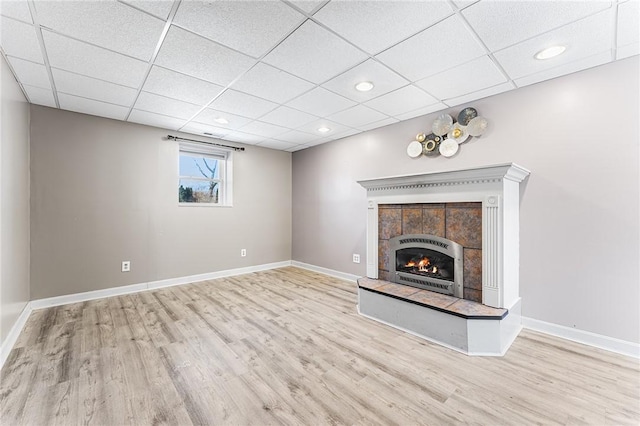 unfurnished living room with a tile fireplace, wood finished floors, a paneled ceiling, and baseboards