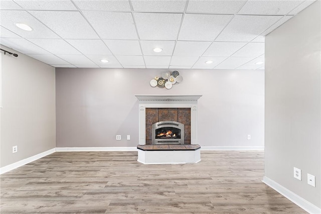 unfurnished living room with a paneled ceiling, recessed lighting, wood finished floors, baseboards, and a tiled fireplace