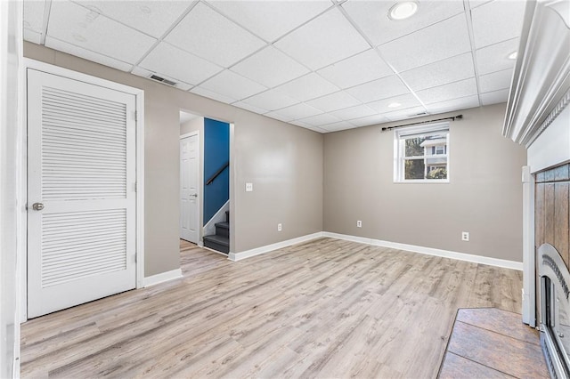 interior space with light wood-style flooring, stairs, baseboards, and a drop ceiling