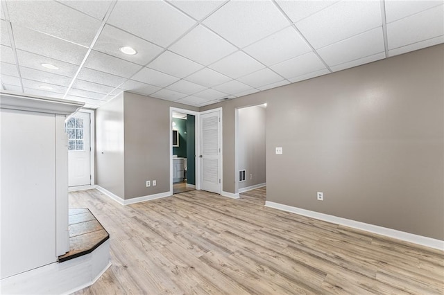 empty room with visible vents, a drop ceiling, light wood-style flooring, and baseboards