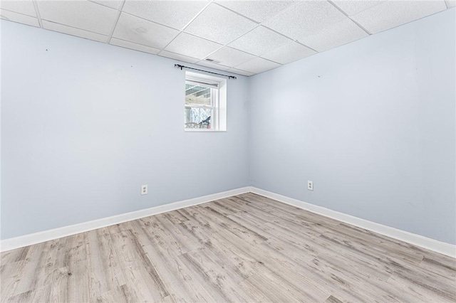 unfurnished room featuring light wood-type flooring, a drop ceiling, and baseboards