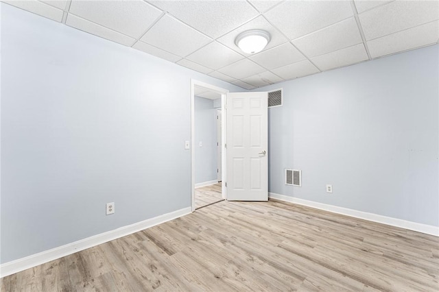 empty room featuring baseboards, visible vents, a drop ceiling, and light wood finished floors