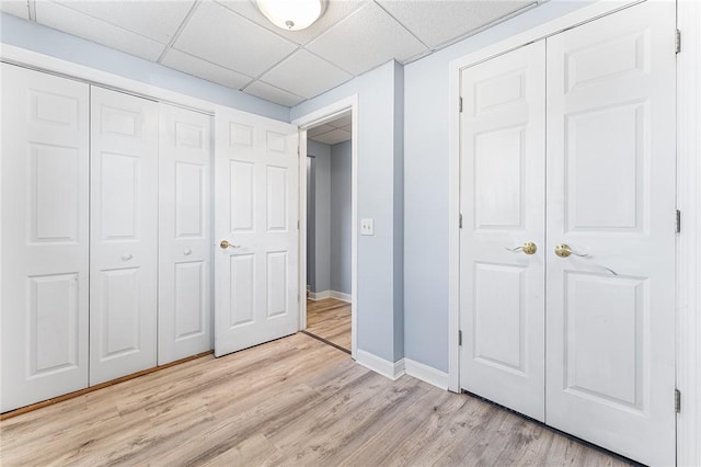 unfurnished bedroom with light wood-type flooring, a closet, baseboards, and a paneled ceiling