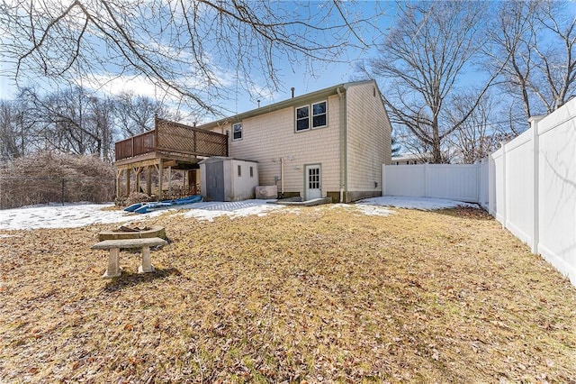 snow covered house with an outdoor structure, a fenced backyard, and a wooden deck