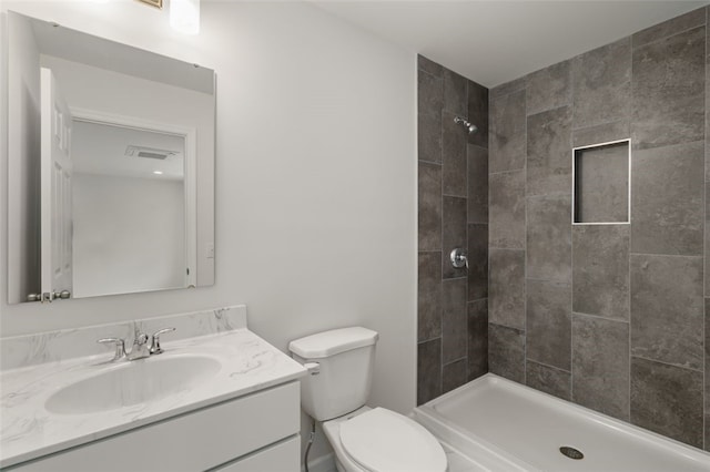 bathroom with vanity, toilet, visible vents, and tiled shower