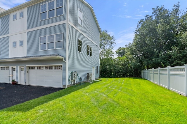 view of side of property featuring aphalt driveway, a garage, a yard, and fence