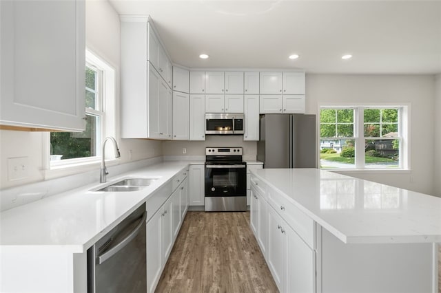 kitchen with recessed lighting, a sink, stainless steel appliances, white cabinets, and a center island