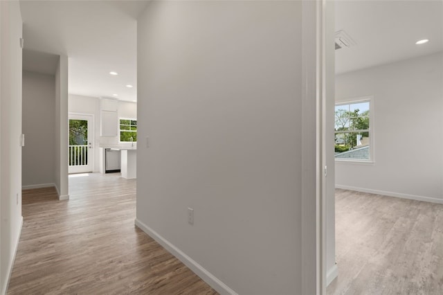 hallway with a wealth of natural light, baseboards, and light wood finished floors