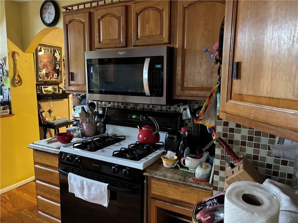 kitchen featuring tasteful backsplash, stainless steel microwave, black gas range, and wood finished floors