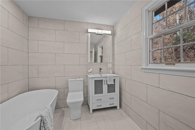 full bath with toilet, a soaking tub, vanity, and tile walls