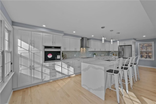 kitchen with tasteful backsplash, appliances with stainless steel finishes, white cabinetry, a sink, and wall chimney range hood