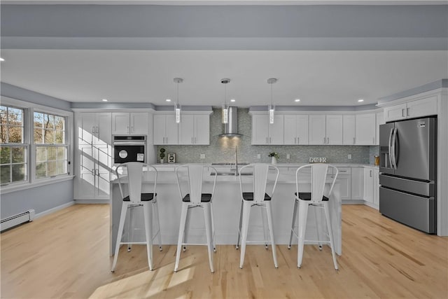 kitchen featuring light wood-style flooring, light countertops, appliances with stainless steel finishes, wall chimney exhaust hood, and tasteful backsplash