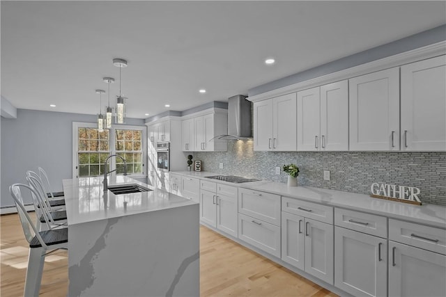 kitchen featuring black electric stovetop, light wood-style flooring, a sink, wall chimney exhaust hood, and tasteful backsplash