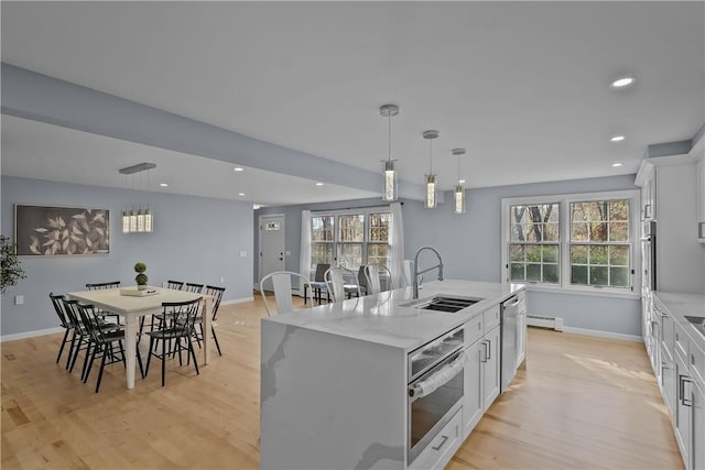 kitchen with a center island with sink, stainless steel appliances, light wood-style flooring, white cabinetry, and a sink