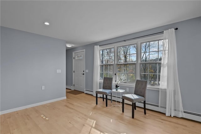 living area with a baseboard radiator, plenty of natural light, baseboards, and wood finished floors