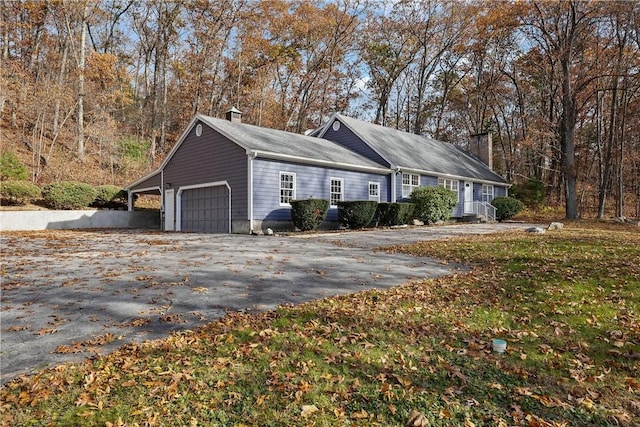 view of front of house with driveway, a chimney, an attached garage, and a front yard