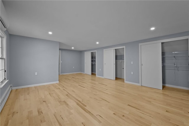 unfurnished bedroom with a baseboard radiator, light wood-style flooring, recessed lighting, baseboards, and multiple closets