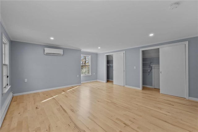 unfurnished bedroom featuring multiple closets, light wood-type flooring, ornamental molding, and an AC wall unit