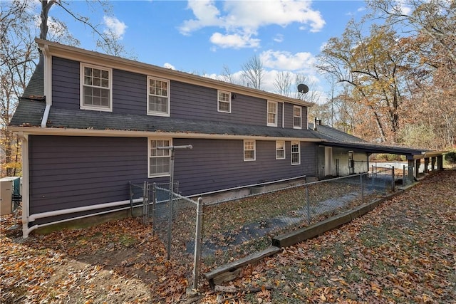 rear view of house with a shingled roof, fence, and a gate