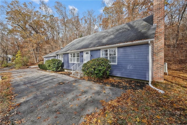 view of front of home featuring aphalt driveway, roof with shingles, and a chimney