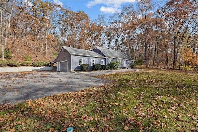 view of home's exterior featuring a chimney, driveway, a lawn, and an attached garage