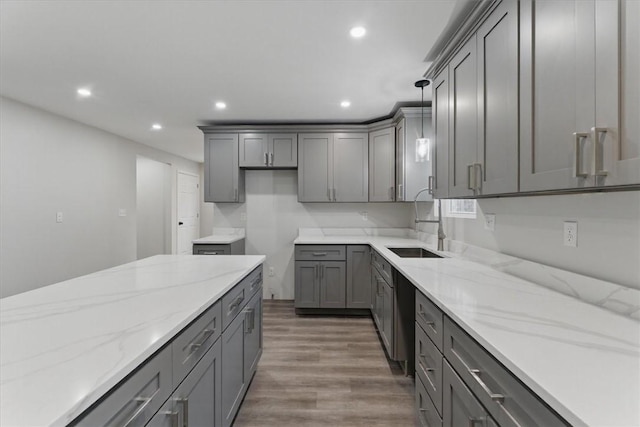 kitchen with wood finished floors, gray cabinets, a sink, and light stone countertops