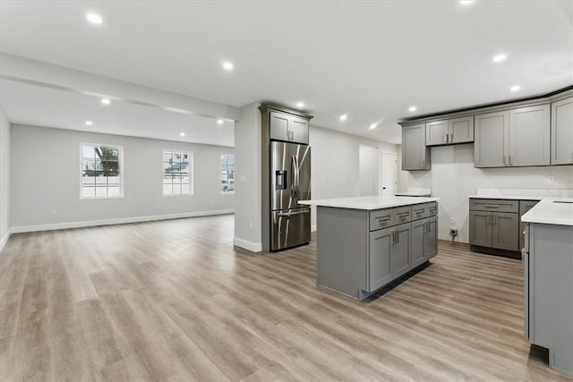 kitchen featuring a kitchen island, open floor plan, gray cabinets, stainless steel fridge with ice dispenser, and light wood finished floors