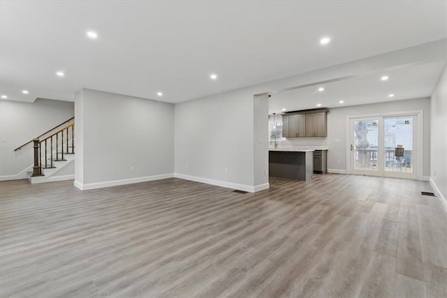 unfurnished living room with light wood finished floors, stairs, baseboards, and recessed lighting