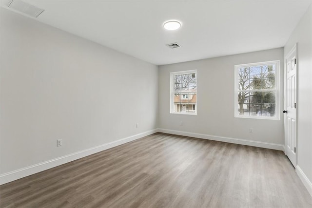 spare room with baseboards, visible vents, and wood finished floors